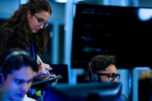 IT technician writing notes while reviewing server room monitors